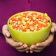 Hands holding a green bowl full of candy corn